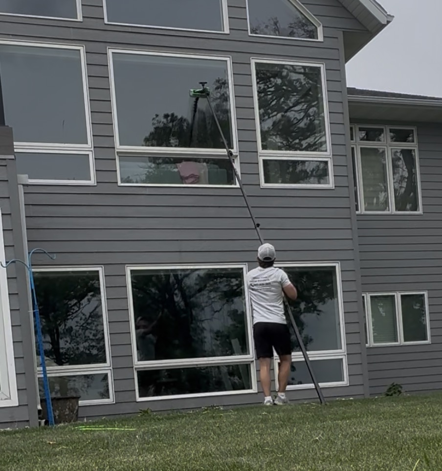 BorderView technician using a water-fed pole to clean tall windows on a two-story home